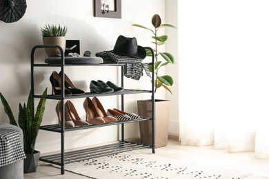 Black shelving unit with shoes and different accessories near white wall in hall