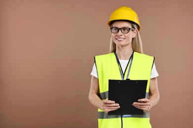 Engineer in hard hat holding clipboard on brown background, space for text