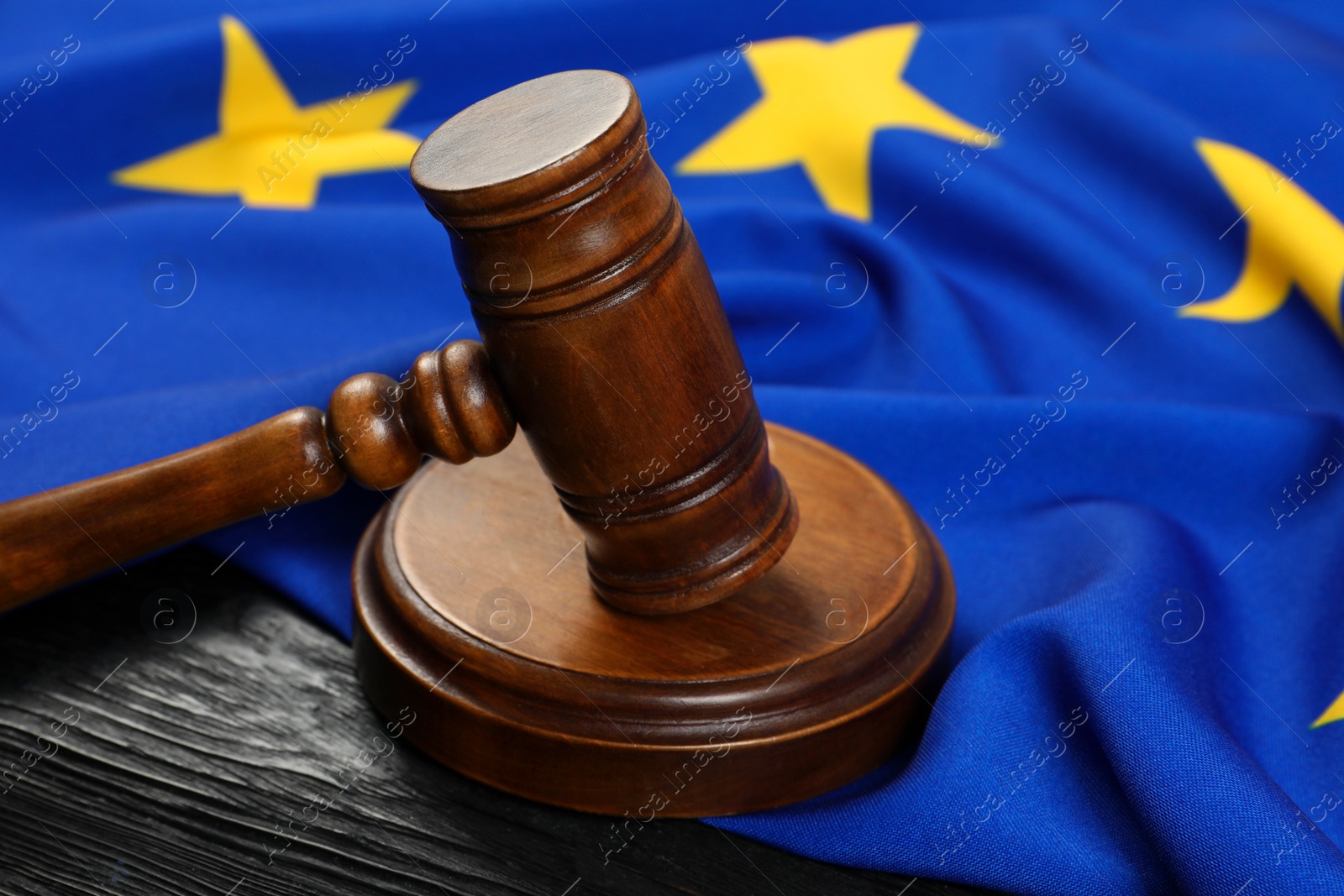 Photo of Judge's gavel and flag of European Union on black wooden table, closeup