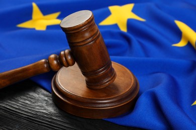 Photo of Judge's gavel and flag of European Union on black wooden table, closeup