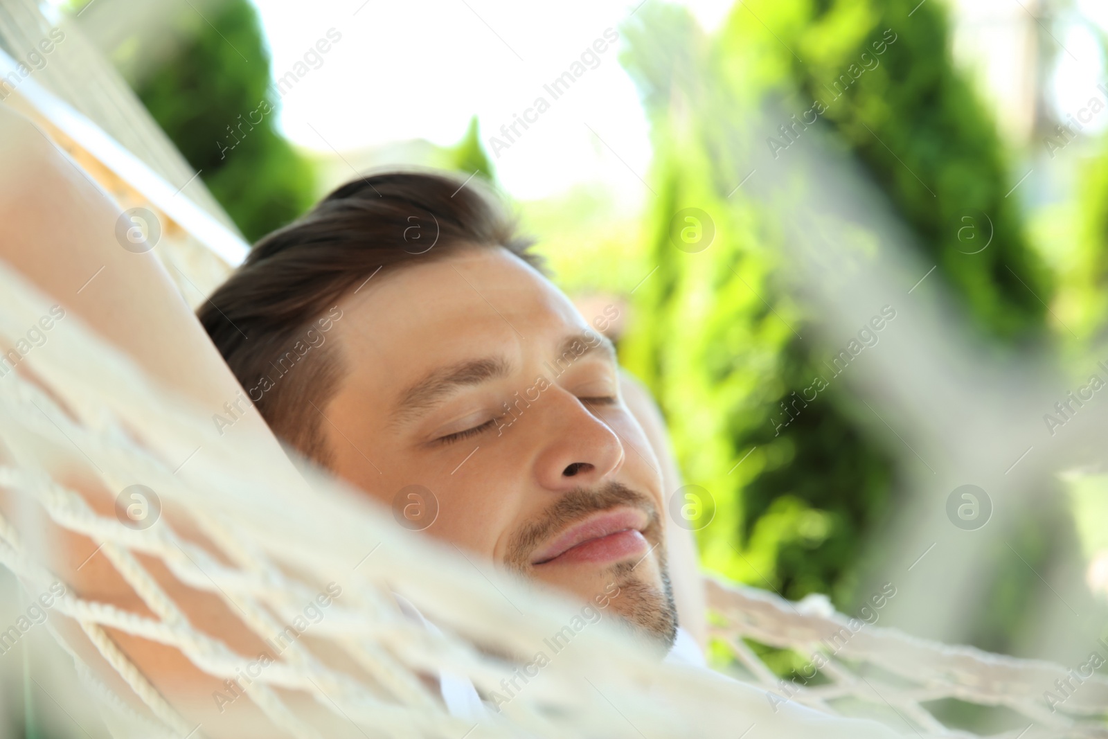 Photo of Man sleeping in hammock outdoors on warm summer day