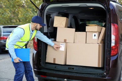 Photo of Young courier checking amount of parcels in delivery van, outdoors