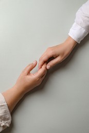 Photo of Woman holding hands with her mother light grey background, top view