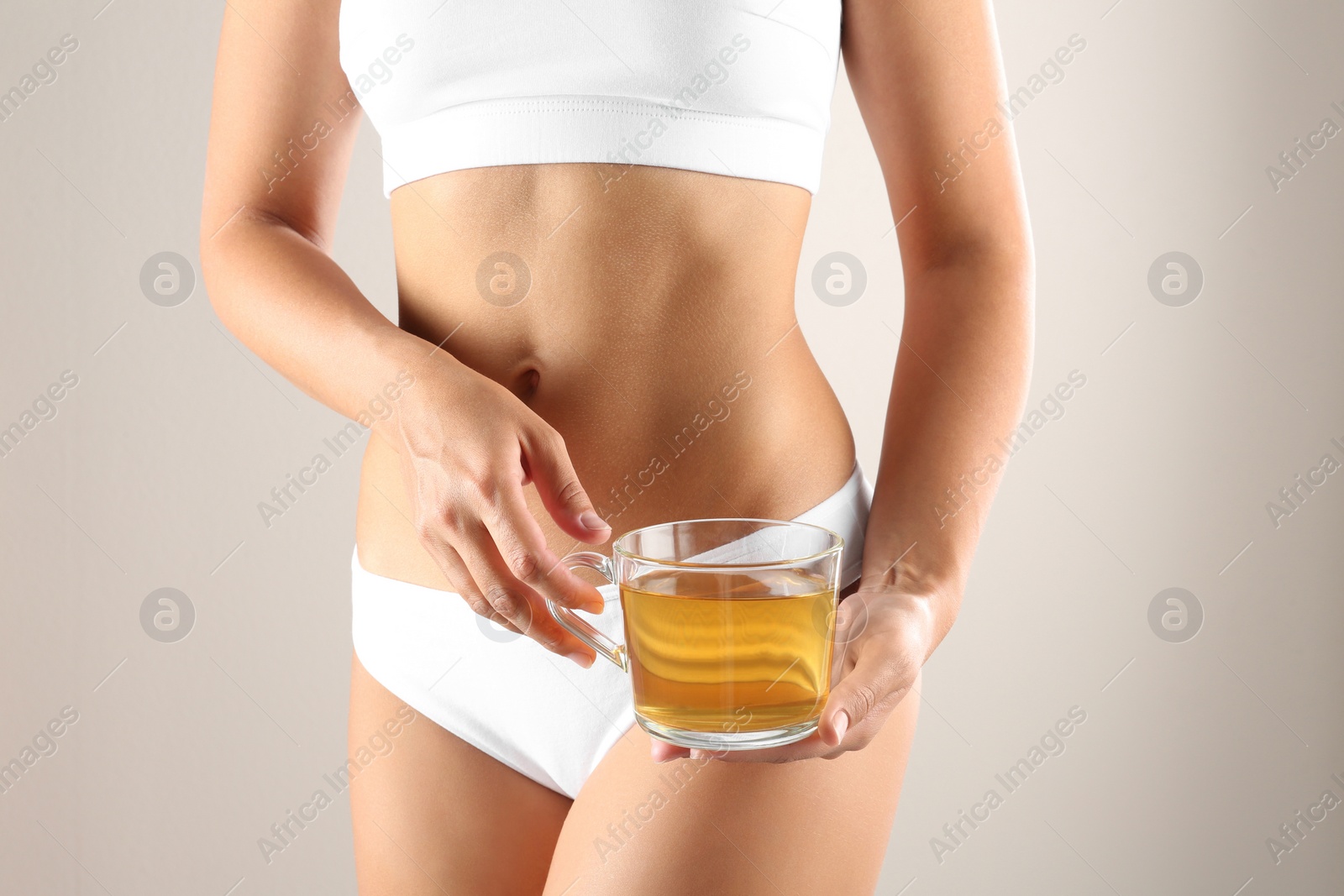 Photo of Young woman holding cup of diet tea on beige background, closeup