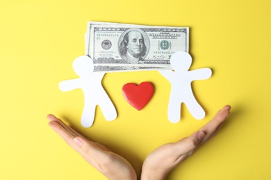 Photo of Woman holding hands near paper silhouettes of people, heart and money bills on color background, top view. Life insurance concept