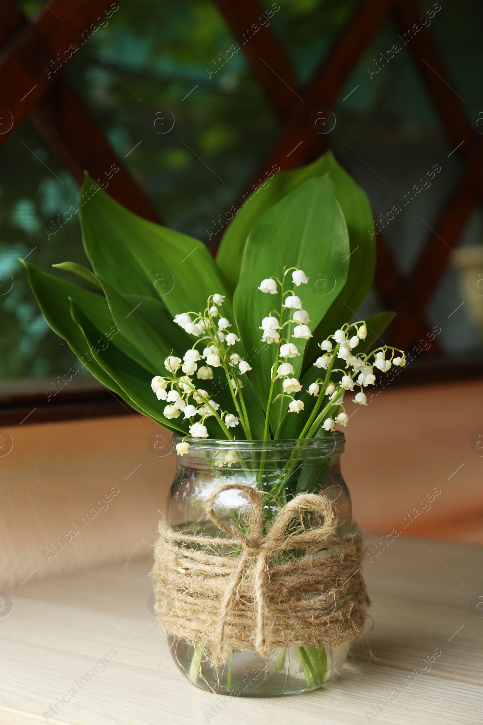 Photo of Beautiful lily of the valley flowers in glass vase on wooden table indoors