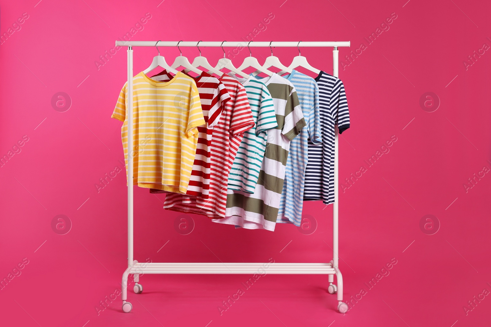 Photo of Colorful clothes hanging on rack against pink background