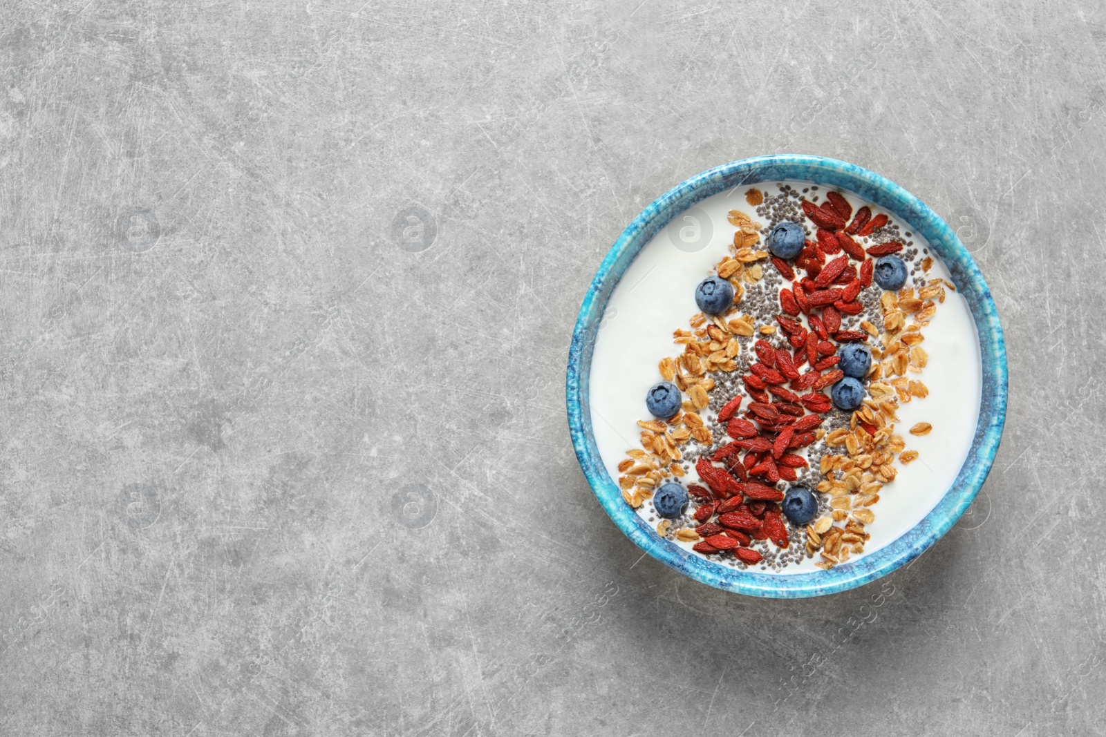 Photo of Smoothie bowl with goji berries on grey table, top view. Space for text