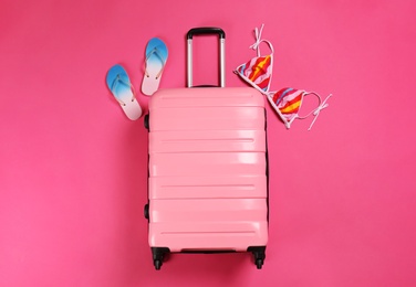 Photo of Stylish suitcase, bikini top and flip flops on color background, top view