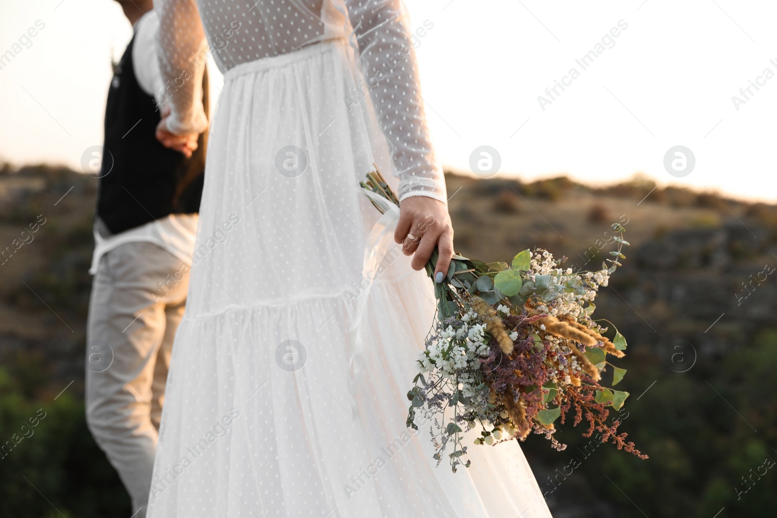 Photo of Happy newlyweds with beautiful field bouquet outdoors, closeup