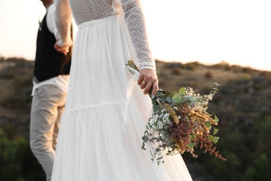 Photo of Happy newlyweds with beautiful field bouquet outdoors, closeup