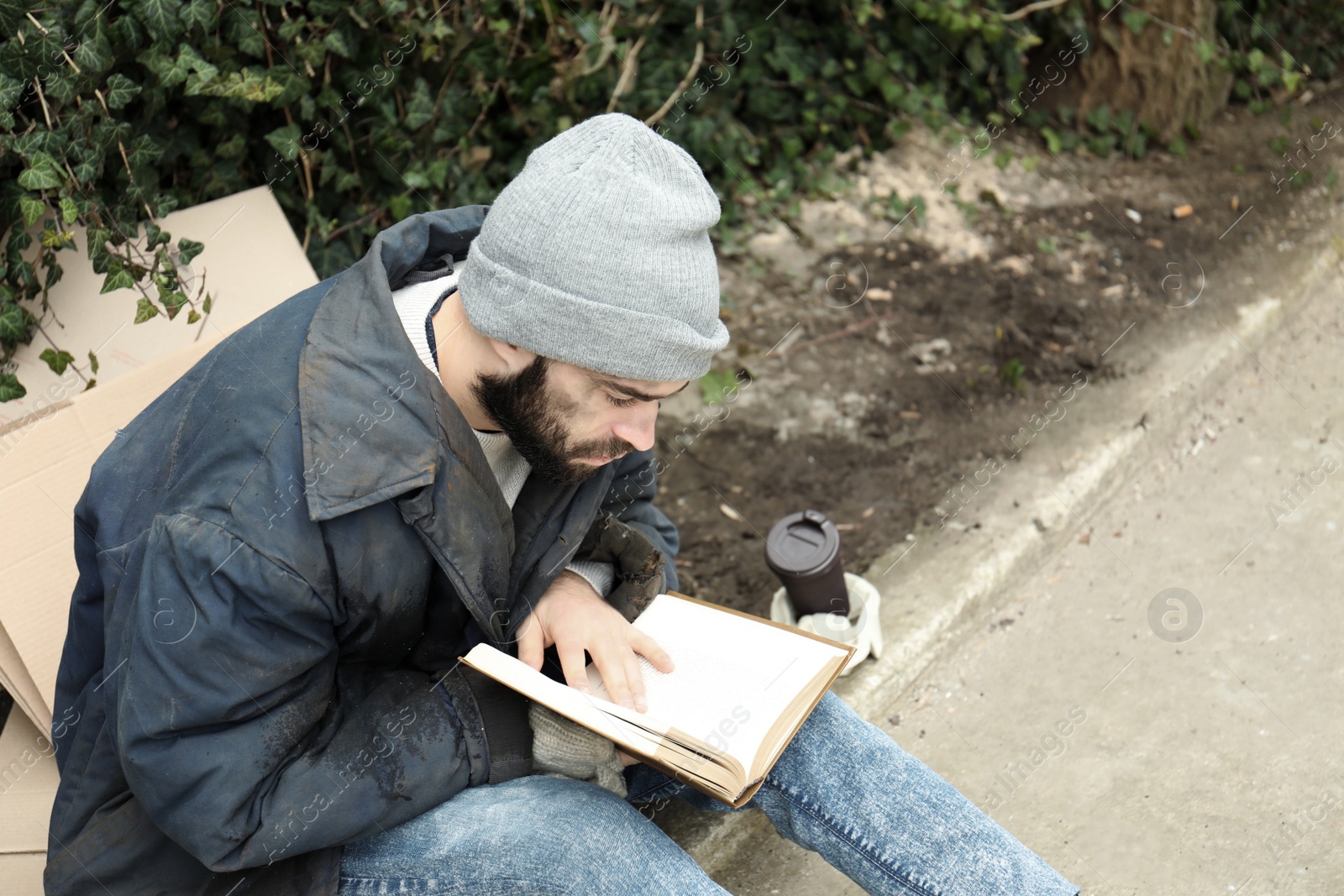 Photo of Poor homeless man with book on street in city