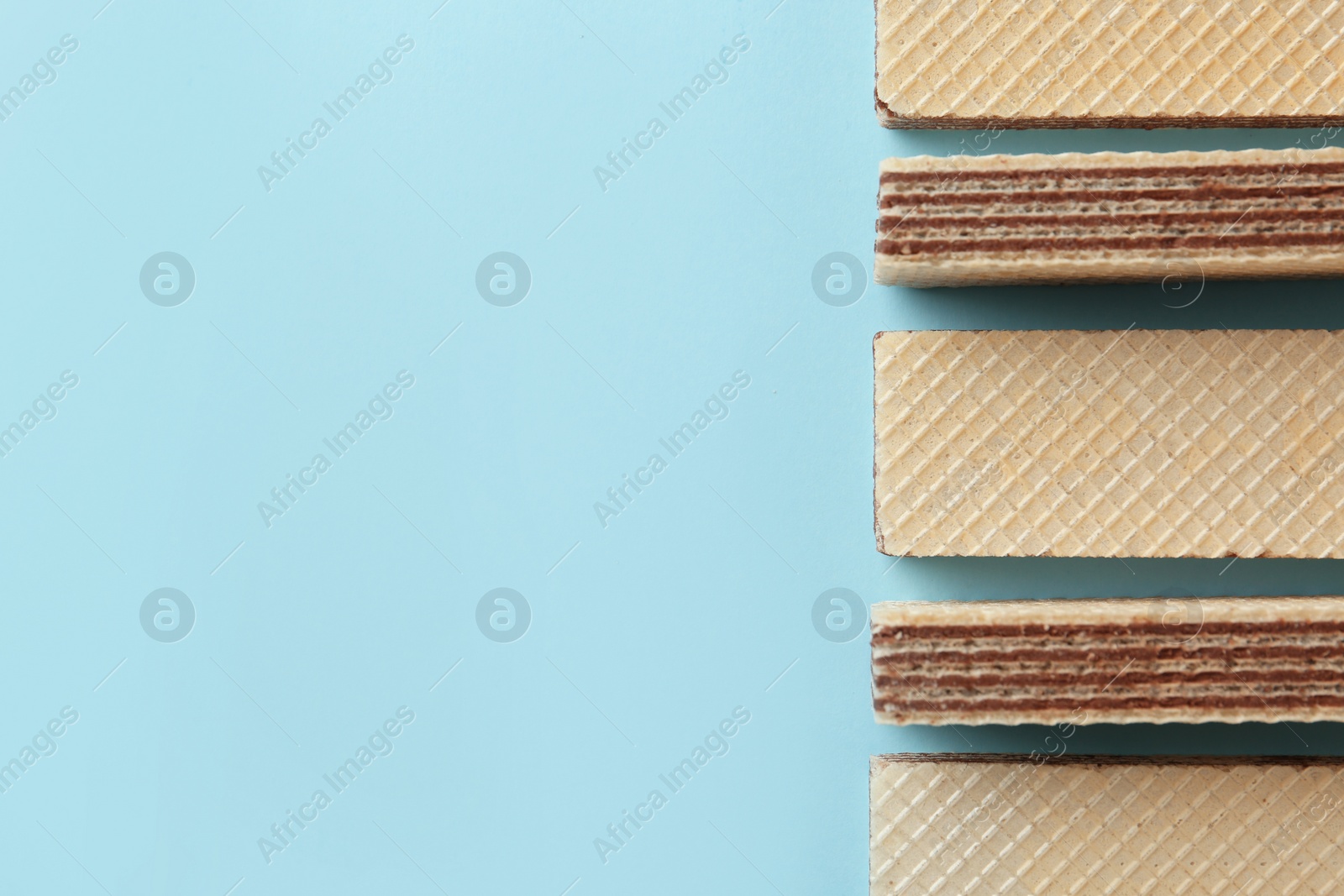 Photo of Tasty wafer sticks on blue background, flat lay with space for text. Sweet food