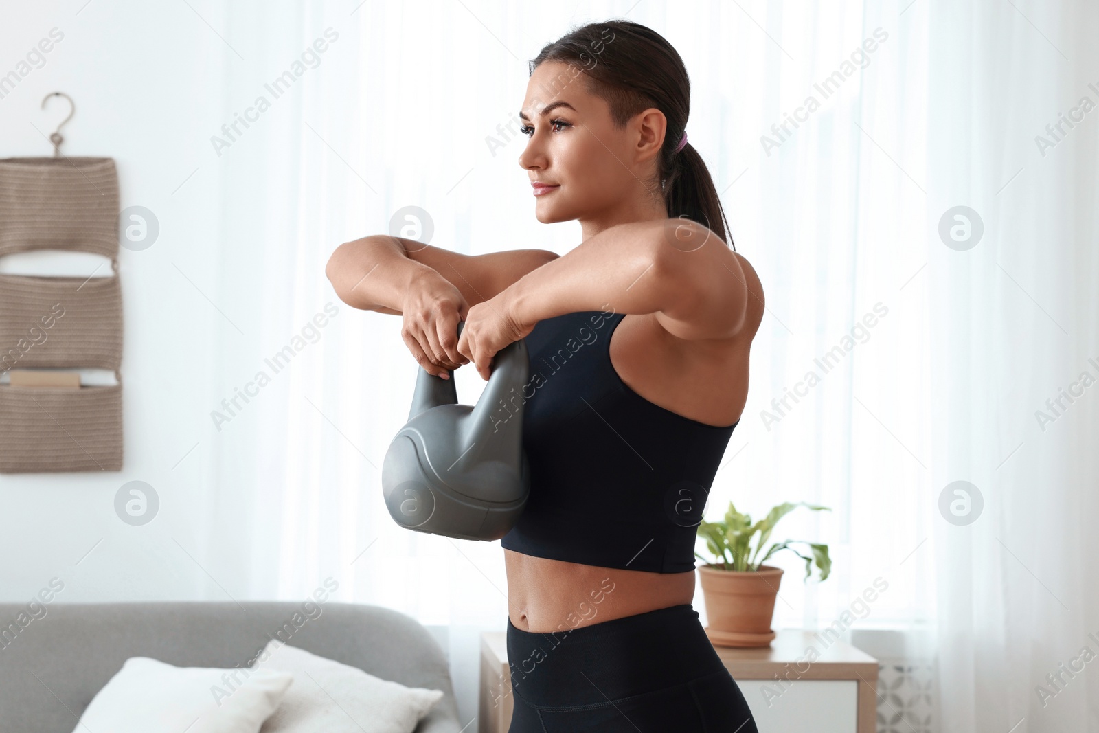 Photo of Young woman exercising with kettlebell at home
