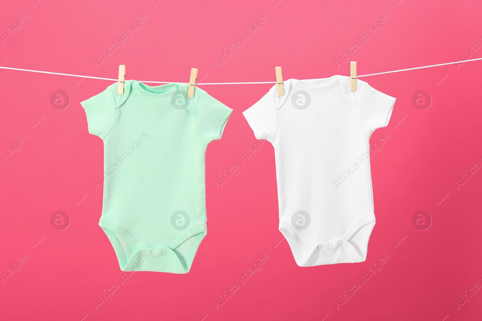 Photo of Baby onesies hanging on clothes line against pink background