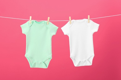 Photo of Baby onesies hanging on clothes line against pink background