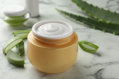 Jar with cream and cut aloe leaves on white marble table, closeup