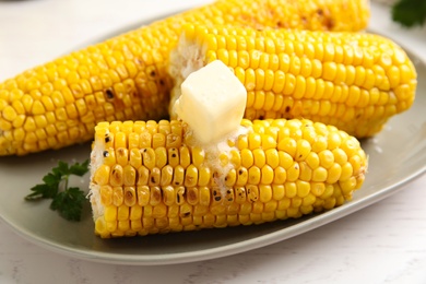 Fresh grilled corn cobs with butter on white wooden table, closeup