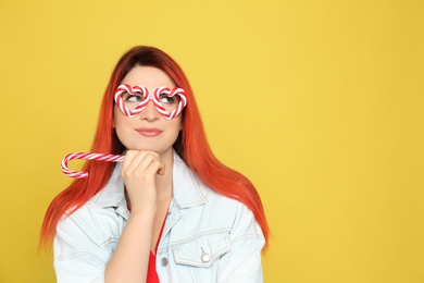 Young woman with bright dyed hair holding candy canes on yellow background. Space for text