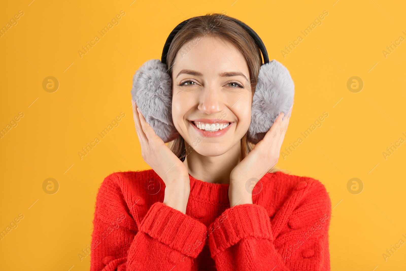 Photo of Happy woman wearing warm earmuffs on yellow background