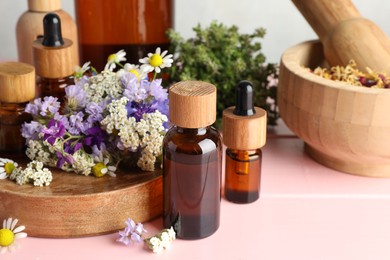 Photo of Aromatherapy. Different essential oils, mortar, pestle and flowers on pink wooden table