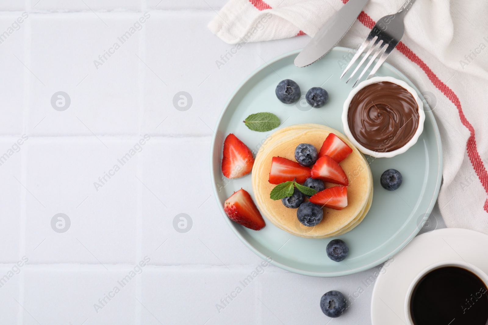 Photo of Delicious pancakes with strawberries, blueberries and chocolate sauce served on white tiled table, flat lay. Space for text