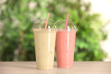 Photo of Plastic cups with different tasty smoothies on wooden table outdoors