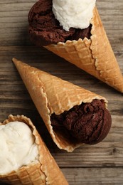 Photo of Ice cream scoops in wafer cones on wooden table, flat lay