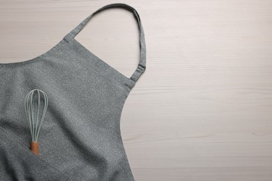 Photo of Stylish apron and whisk on white wooden table, top view. Mockup for design
