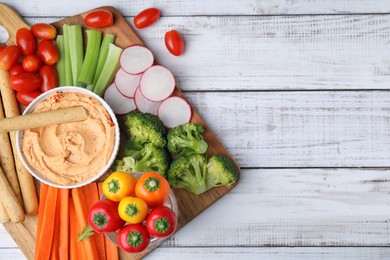 Photo of Board with delicious hummus, grissini sticks and fresh vegetables on white wooden background, top view. Space for text