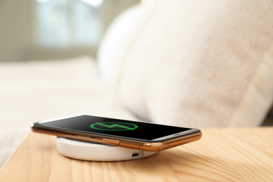 Photo of Modern mobile phone charging on wireless pad in bedroom, closeup