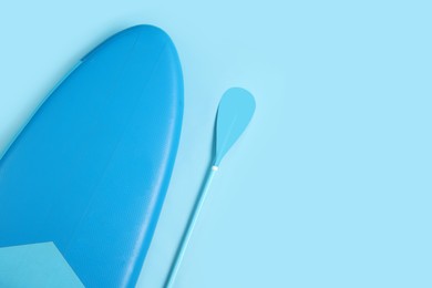 Photo of Board and paddle for standup paddleboarding (SUP) on light blue background, flat lay. Space for text