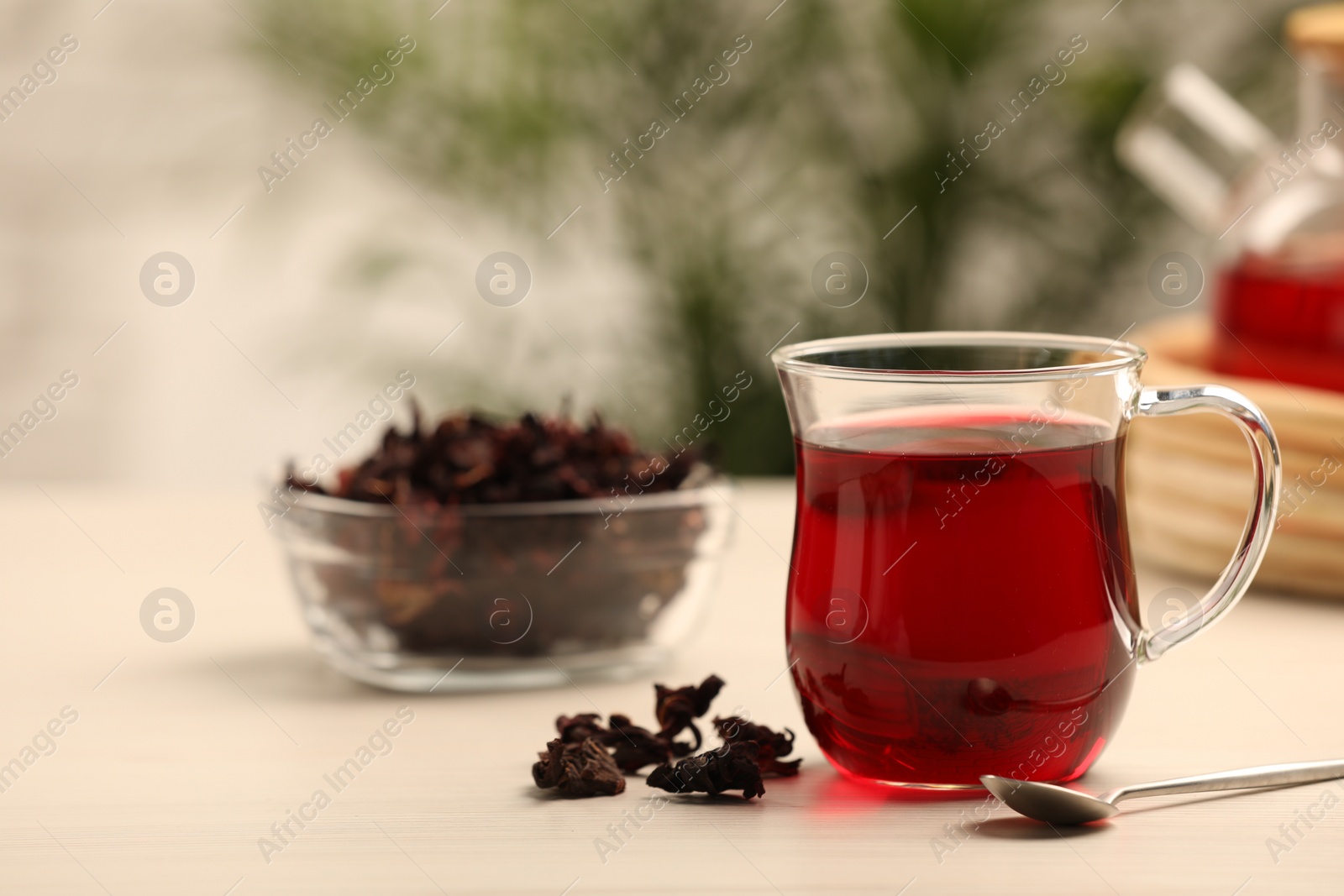 Delicious hibiscus tea and dry flowers on white wooden table, space for text Photo of Delicious hibiscus tea and dry flowers on white wooden table, space for text