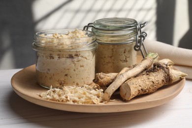 Photo of Platter with tasty prepared horseradish and roots on white wooden table, closeup