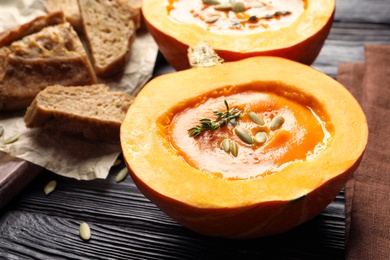 Photo of Tasty cream soup served in pumpkin on wooden table