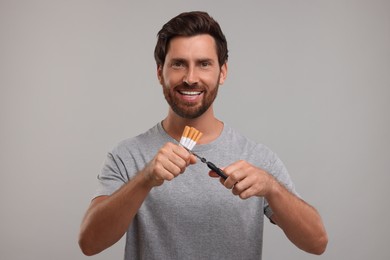 Photo of Stop smoking concept. Man cutting cigarettes on grey background