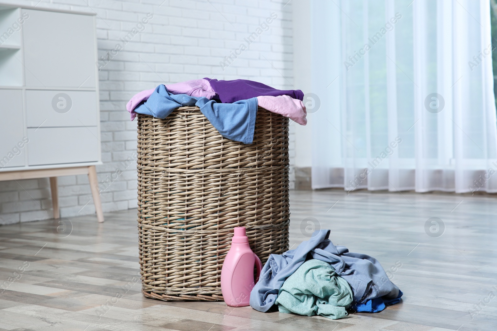 Photo of Laundry basket with dirty clothes and detergent on floor in room