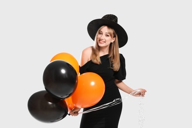 Photo of Beautiful woman in witch costume with balloons on white background. Halloween party