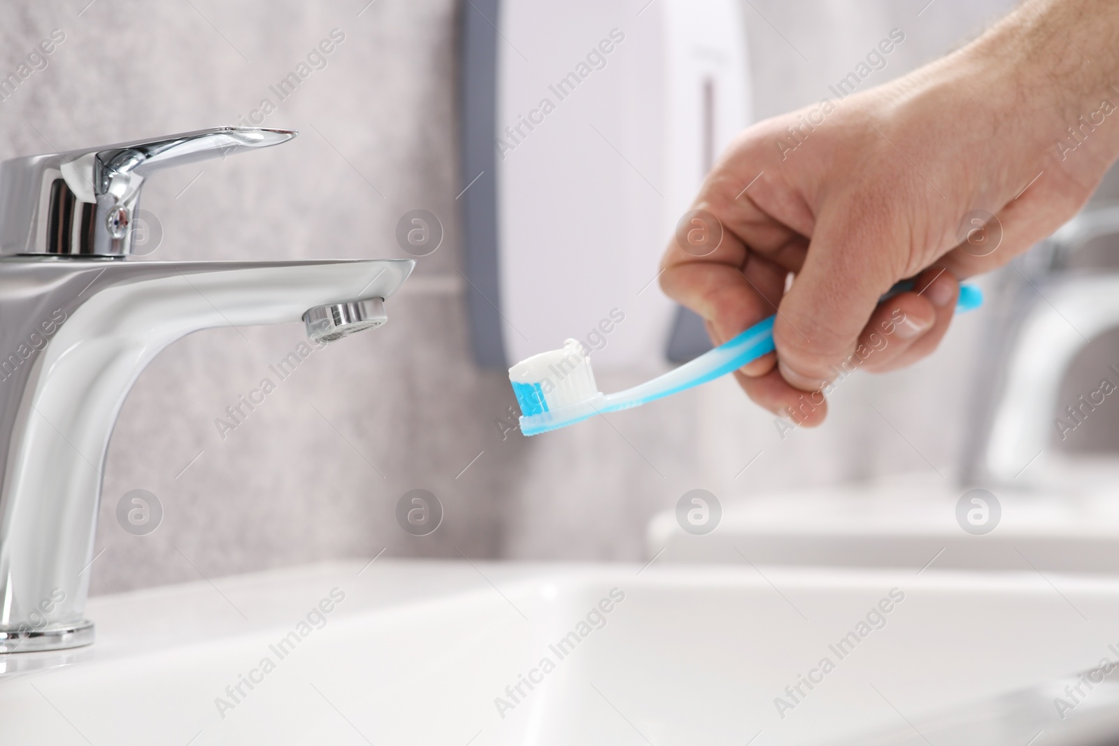 Photo of Man holding toothbrush with paste above sink in bathroom, closeup