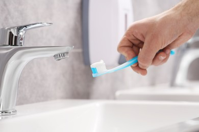 Photo of Man holding toothbrush with paste above sink in bathroom, closeup