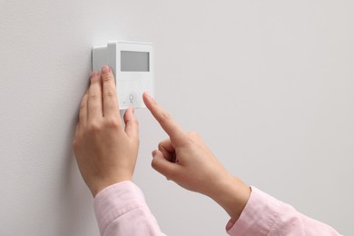 Photo of Woman adjusting thermostat on white wall, closeup. Smart home system