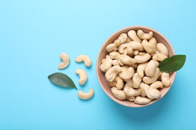 Photo of Many tasty cashew nuts and leaves on light blue background, top view. Space for text