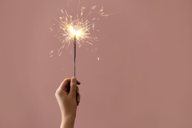 Photo of Woman holding burning sparklers on pink background, closeup. Space for text