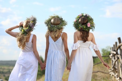 Photo of Young women wearing wreaths made of beautiful flowers outdoors on sunny day, back view