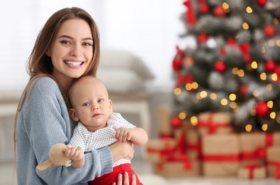 Photo of Happy mother with cute baby in room decorated for Christmas holiday