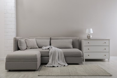 Photo of Large grey sofa and chest of drawers near light wall in room. Interior design