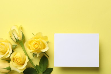 Photo of Beautiful roses and blank card on yellow background, flat lay. Space for text