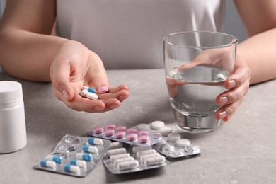 Photo of Woman with different pills and glass of water at grey table, closeup