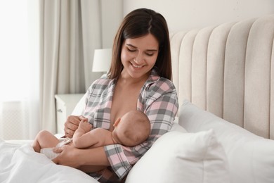 Photo of Young woman breastfeeding her little baby on bed at home