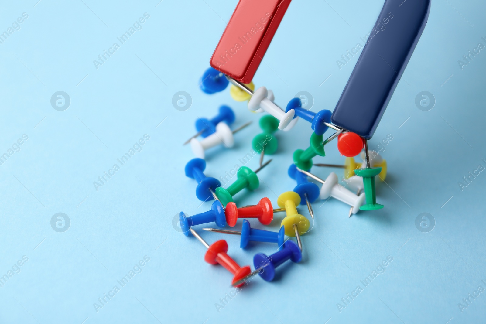 Photo of Magnet attracting colorful pins on light blue background, closeup
